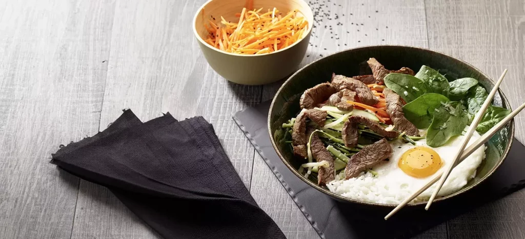 Bibimbap avec bœuf émincé, riz, œuf au plat, légumes et herbes fraîches.