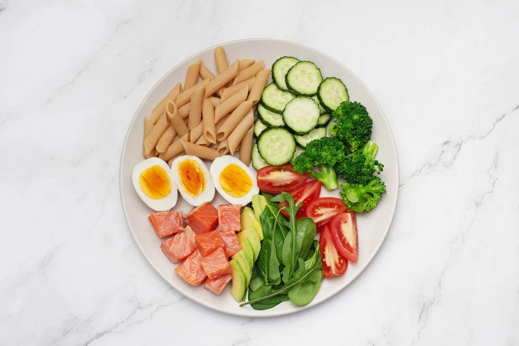 Assiette équilibrée avec pâtes complètes, saumon, œuf, avocat et légumes frais
