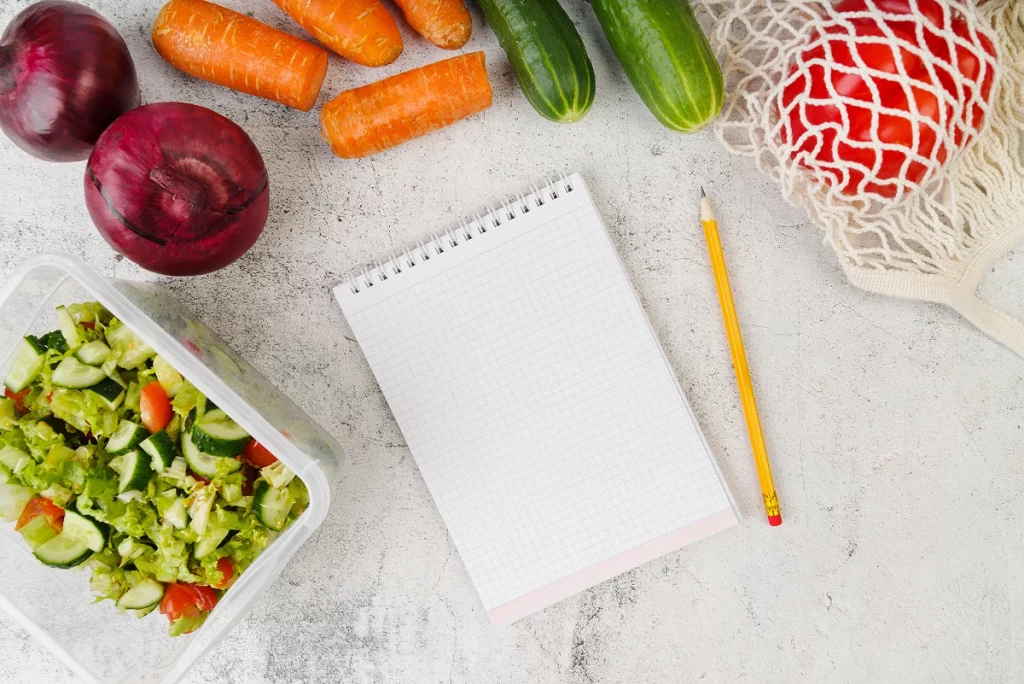 Carnet pour planifier ses repas entouré de légumes frais et salade
