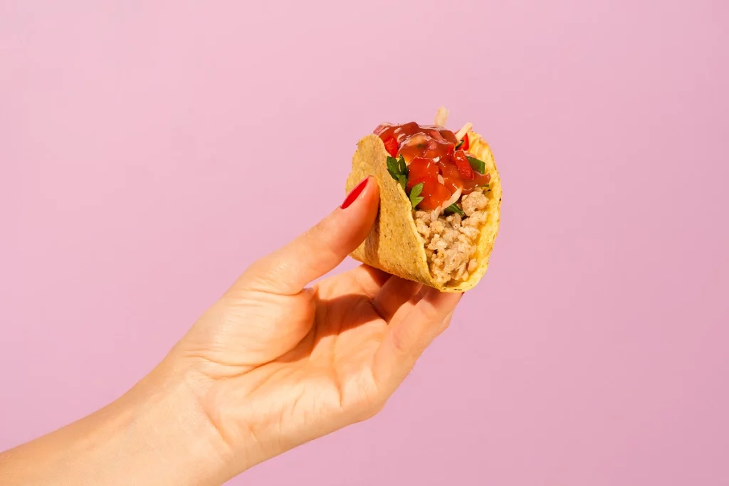 Taco garni de viande hachée, légumes et sauce tenu à la main.