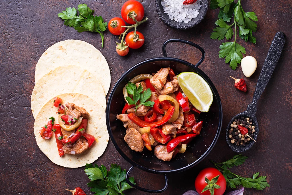 Préparation de tacos avec viande sautée, poivrons, citron vert et tortillas.