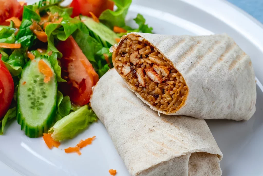 Burrito coupé avec riz et poulet accompagné d’une salade fraîche.