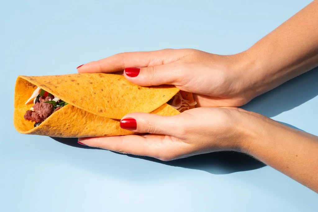 Taco garni de bœuf et légumes tenu entre deux mains.